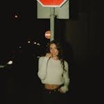 Casual portrait of a woman at night standing beneath a stop sign.