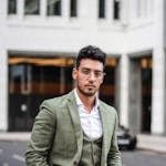 Elegant businessman in a green suit posing confidently on a city street with an urban background.